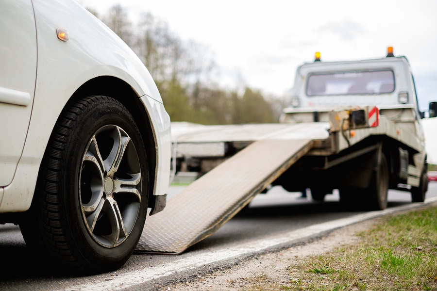 Loading broken car on a tow truck on a roadside white car being towed